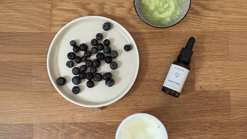 Blaubeeren auf einem Teller, eine Flasche mit Tropfer, eine Schüssel mit grüner Paste und ein Behälter mit Sahne auf einer Holzoberfläche.