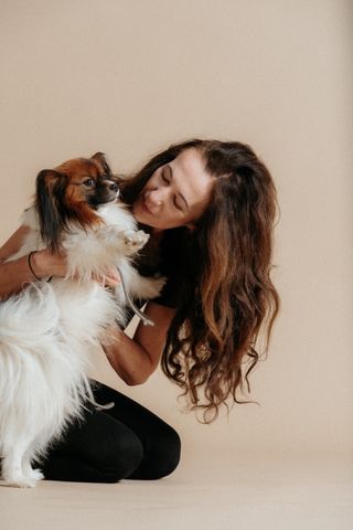 Frau mit langen Haaren hält liebevoll einen flauschigen Hund im Arm
