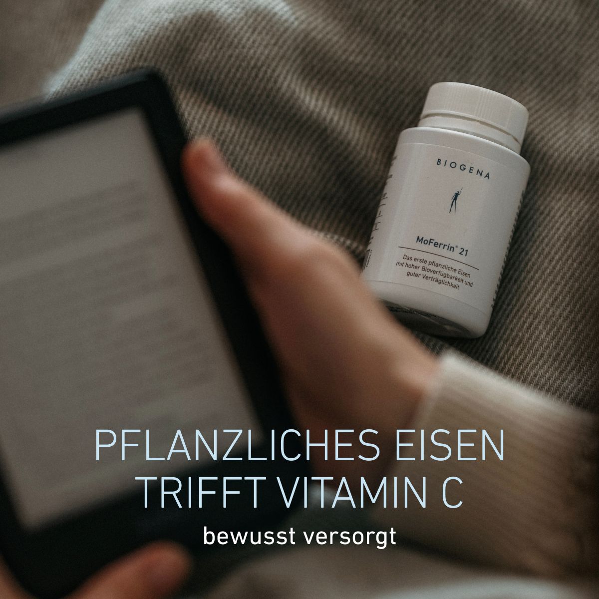 Fľaša BIOGENA MoFerrin 21 položená na látke vedľa osoby držiacej tablet. Železo rastlinného pôvodu v kombinácii s vitamínom C pre uvedomelé stravovanie.