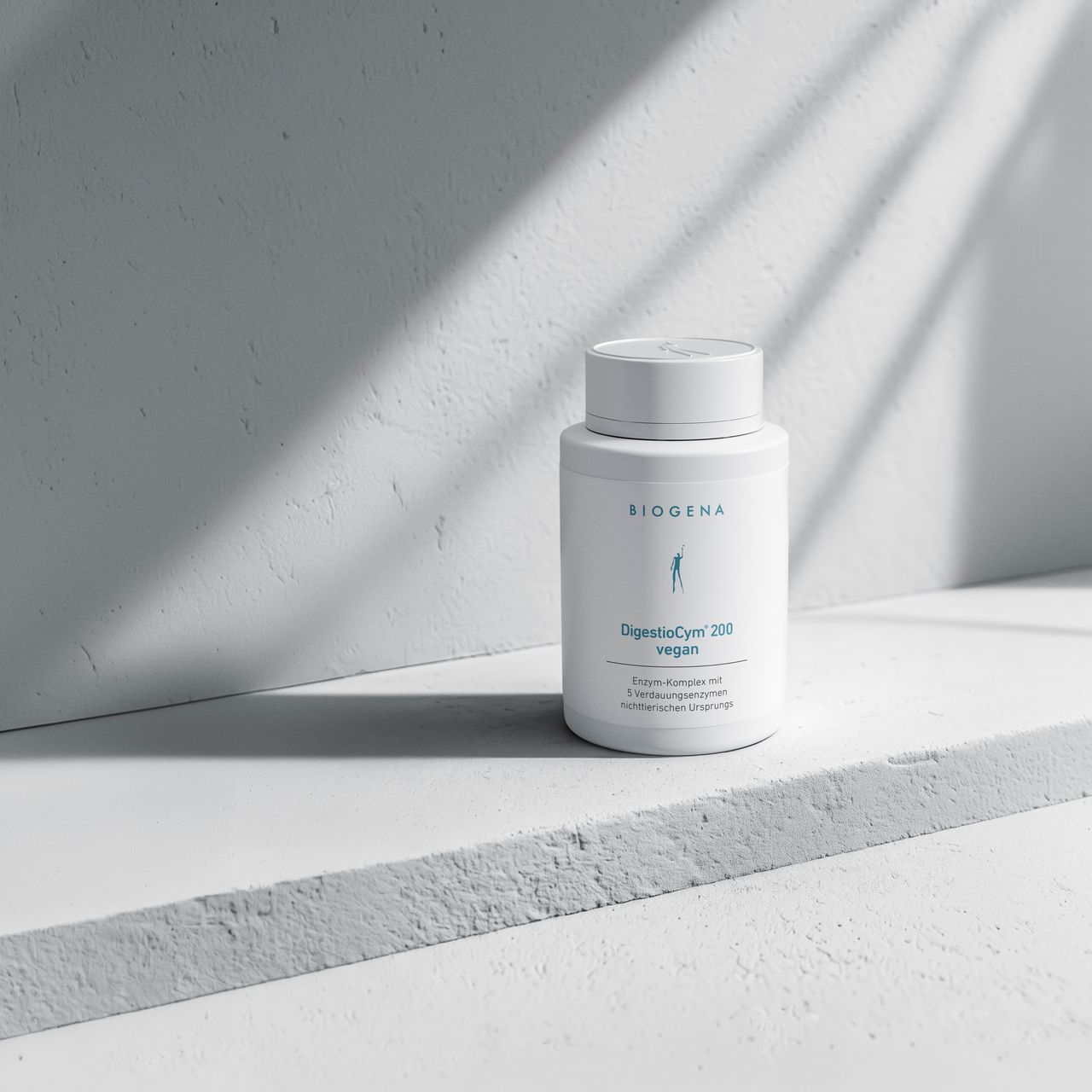 Biogena DigestioCym 200 vegan Dose, weiße Oberfläche, graue Wand, Licht- und Schattenspiel