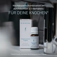 Confezione e flacone delle gocce BIOGENA Vitamina D₃ & K₂ su un piano d'appoggio. Il testo evidenzia la combinazione ad alto dosaggio in rapporto 2:1 e il contributo delle vitamine D e K al mantenimento di ossa normali.