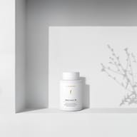 BIOGENA Omni Lactis 20 su uno scaffale bianco minimalista con ombre morbide proiettate da una pianta sullo sfondo.
