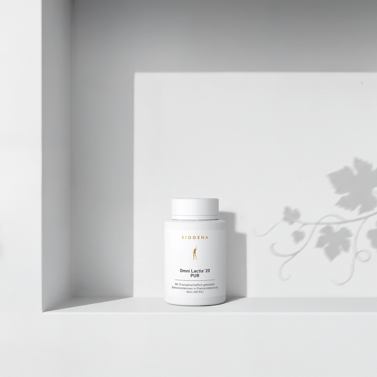 BIOGENA Omni Lactis 20 PUR on a minimalist white shelf with soft shadows cast by a plant in the background.