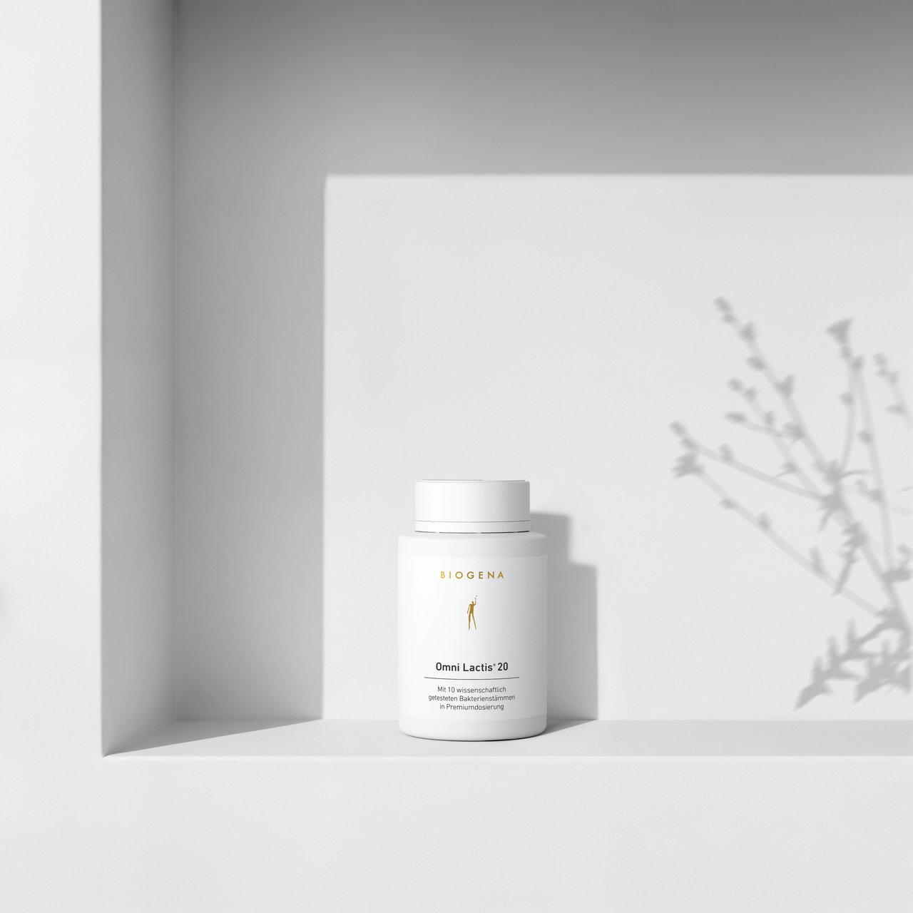 BIOGENA Omni Lactis 20 pe o etajeră albă minimalistă, cu umbre ușoare proiectate de o plantă în fundal.