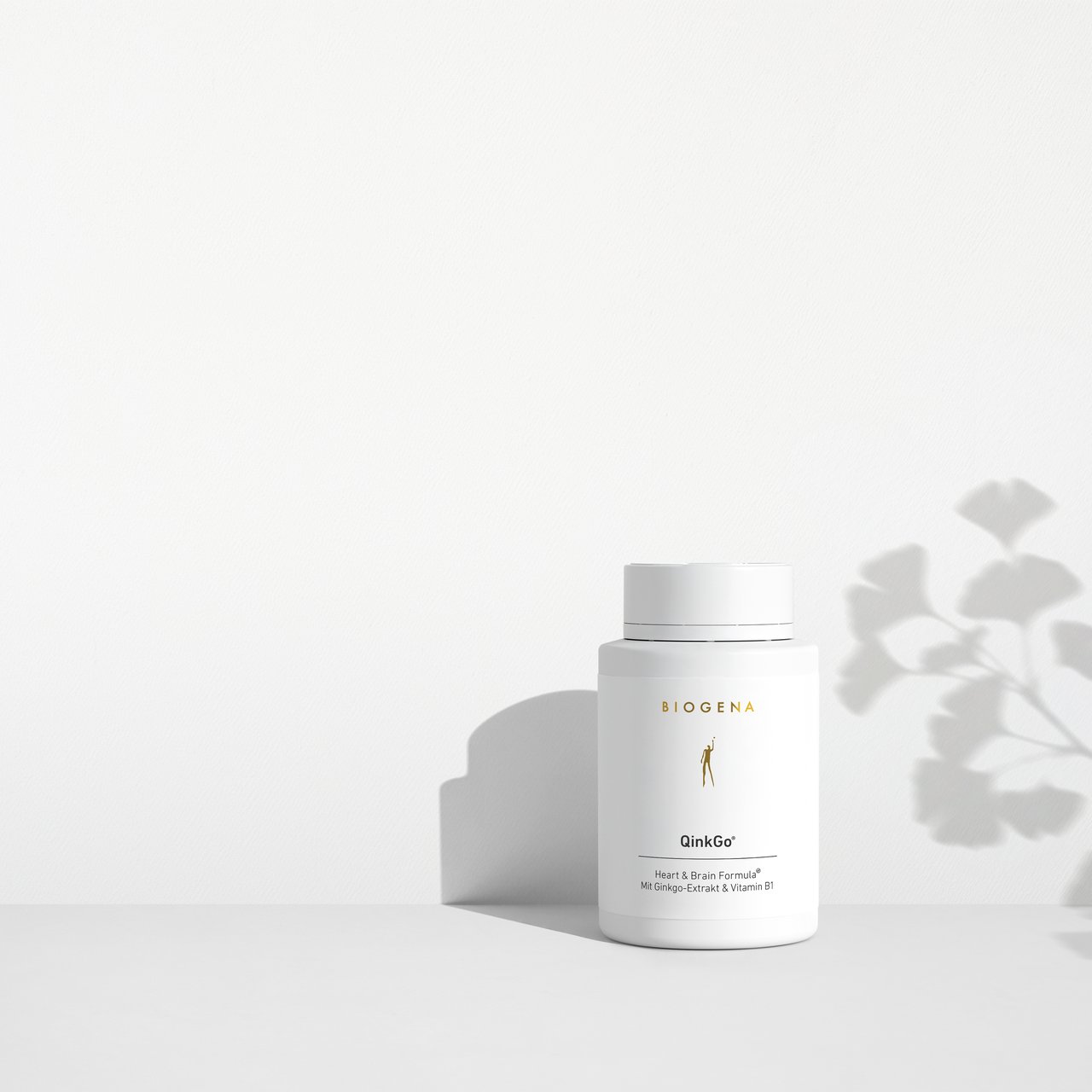 Supliment BIOGENA QinkGo® într-un flacon alb pe fundal minimalist cu lumină și umbră. Formula Heart & Brain cu extract de ginkgo și vitamina B1 pentru susținerea inimii și a creierului.