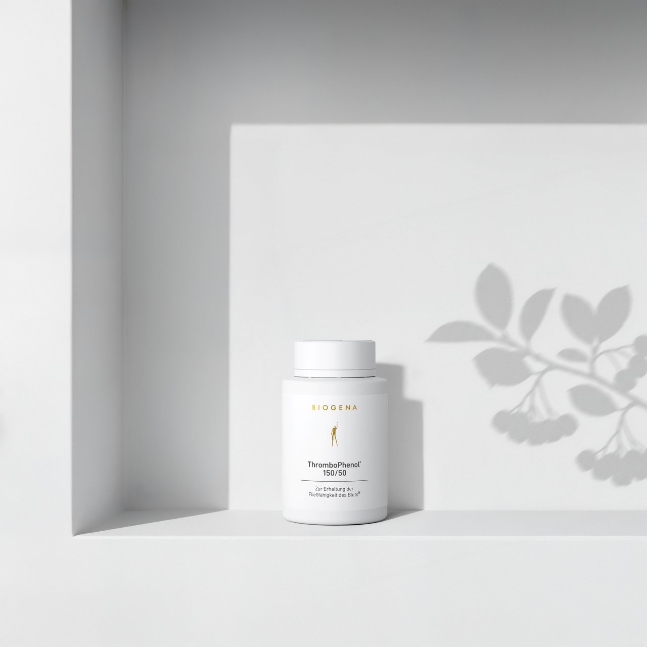 BIOGENA ThromboPhenol 150/50 într-o sticlă albă, așezată pe un raft, cu umbre de plante în fundal. Eticheta conține textul "Pentru menținerea fluidității sângelui."