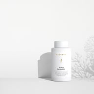 BIOGENA Arthro Formula 4 in einer weißen Flasche, abgestellt auf einer Fläche, mit Schatten von Pflanzen im Hintergrund. Der Text „Premiumpräparat für die Erhaltung der Gelenkfunktionen“ ist auf dem Etikett abgedruckt.