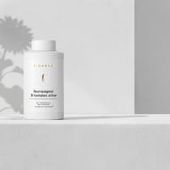 BIOGENA Neurosagena® B-Komplex active on a minimalist white shelf with soft shadows from a flower in the background.
