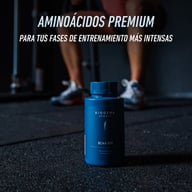 Biogena Sports BCAA 500 botella, envase azul en el suelo, persona con barra en gimnasio