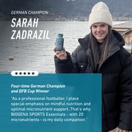 Piłkarka Sarah Zadrazil trzyma Biogena Sports Essentials na tle jeziora i gór. Grafika przedstawia jej rekomendację produktu jako codziennego wsparcia mikroskładnikami dla profesjonalnych sportowców.