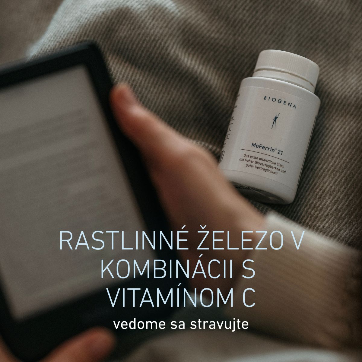 Fľaša BIOGENA MoFerrin 21 položená na látke vedľa osoby držiacej tablet. Železo rastlinného pôvodu v kombinácii s vitamínom C pre uvedomelé stravovanie.